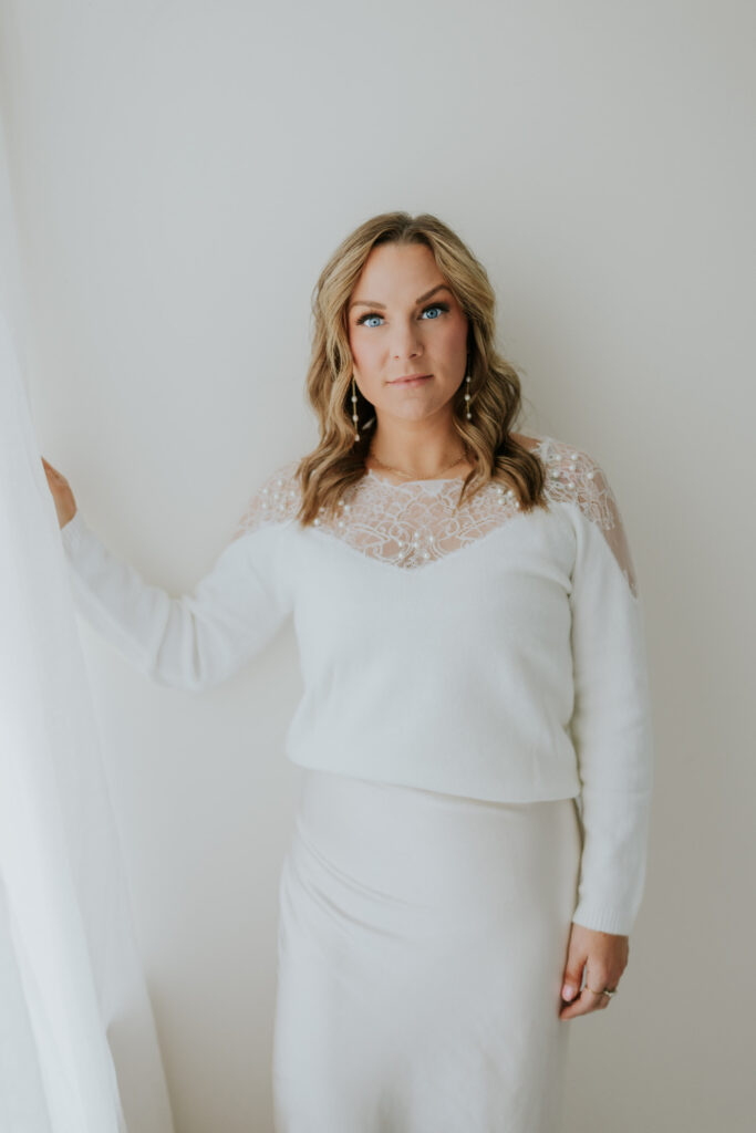 Woman in white lace top poses confidently indoors.