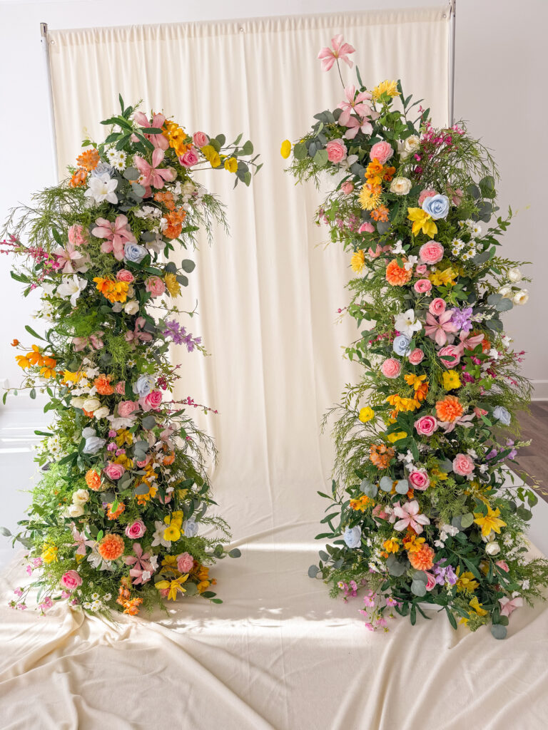 Colorful floral arch arrangement with white curtain backdrop.